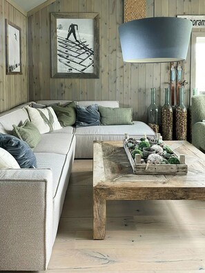 Ein gemütliches Wohnzimmer mit Holzboden, einem grauen Sofa mit Kissen, einem Couchtisch mit Dekoration und einer großen Lampe.