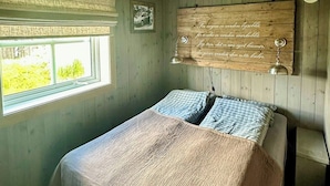 Un dormitorio con cama, ventana, cabecera de madera con texto y una lámpara colgante.