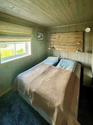 Ein Schlafzimmer mit einem Bett, einem Fenster, einem hölzernen Kopfende mit Text und einer Hängelampe.