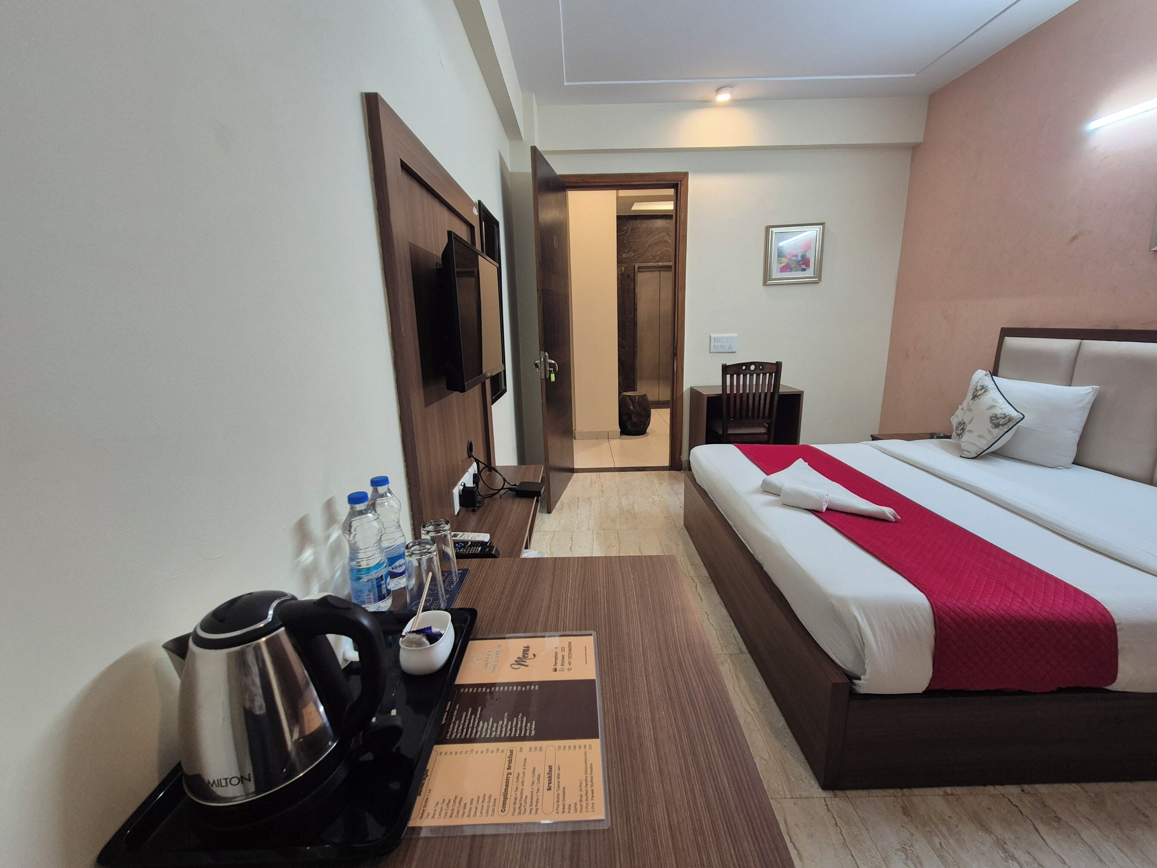 Una habitación de hotel con cama, mesita de noche, silla, televisión y minibar.