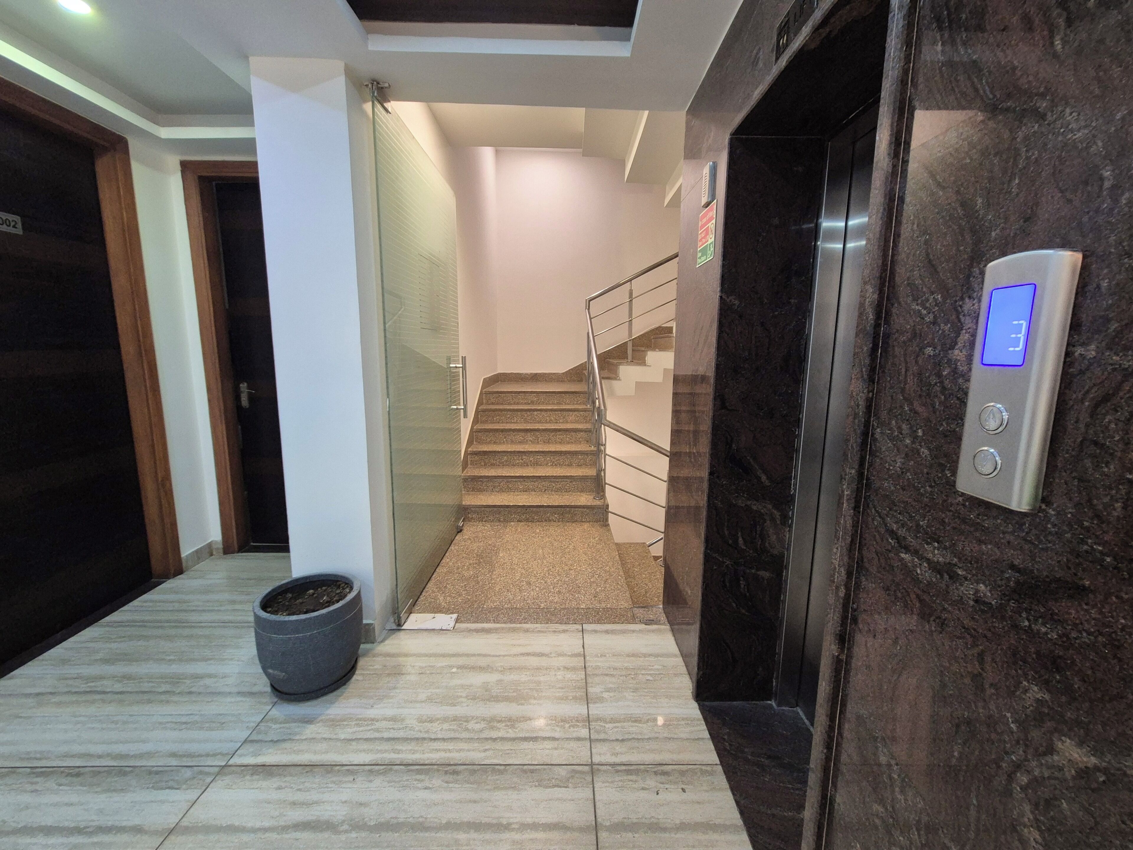 Un intérieur moderne avec un sol en marbre, un escalier, une porte en verre et un ascenseur.