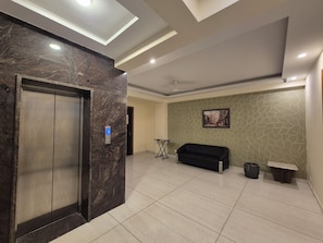 Um hall de entrada com elevador de mármore, um sofá preto, uma pequena mesa e um quadro na parede.
