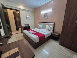 Quarto de hotel com cama, mesas de cabeceira, escrivaninha, cadeira e guarda-roupa.
