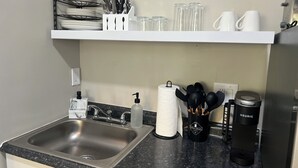 Een keuken met een roestvrijstalen spoelbak, een wit aanrecht, een zwarte koffiezetapparaat en een Keurig koffiezetapparaat.