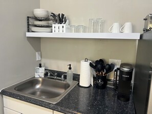 Eine Küche mit Spüle aus Edelstahl, einer weißen Arbeitsplatte, einer schwarzen Kaffeemaschine und einer Keurig-Kaffeemaschine.
