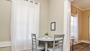 Een kleine eethoek met een ronde tafel en twee stoelen, een potplant en een bord met een welkomstboodschap aan de muur.