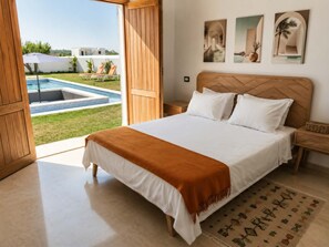 Ein Schlafzimmer mit Bett, Nachttisch, Holz-Kopfteil und Blick auf einen Swimmingpool und Sitzgelegenheiten im Freien.