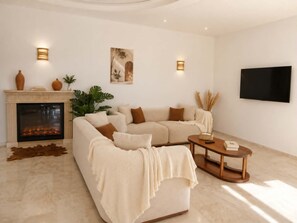 Ein Wohnzimmer mit Kamin, Sofa, Couchtisch und an der Wand befestigtem Fernseher.