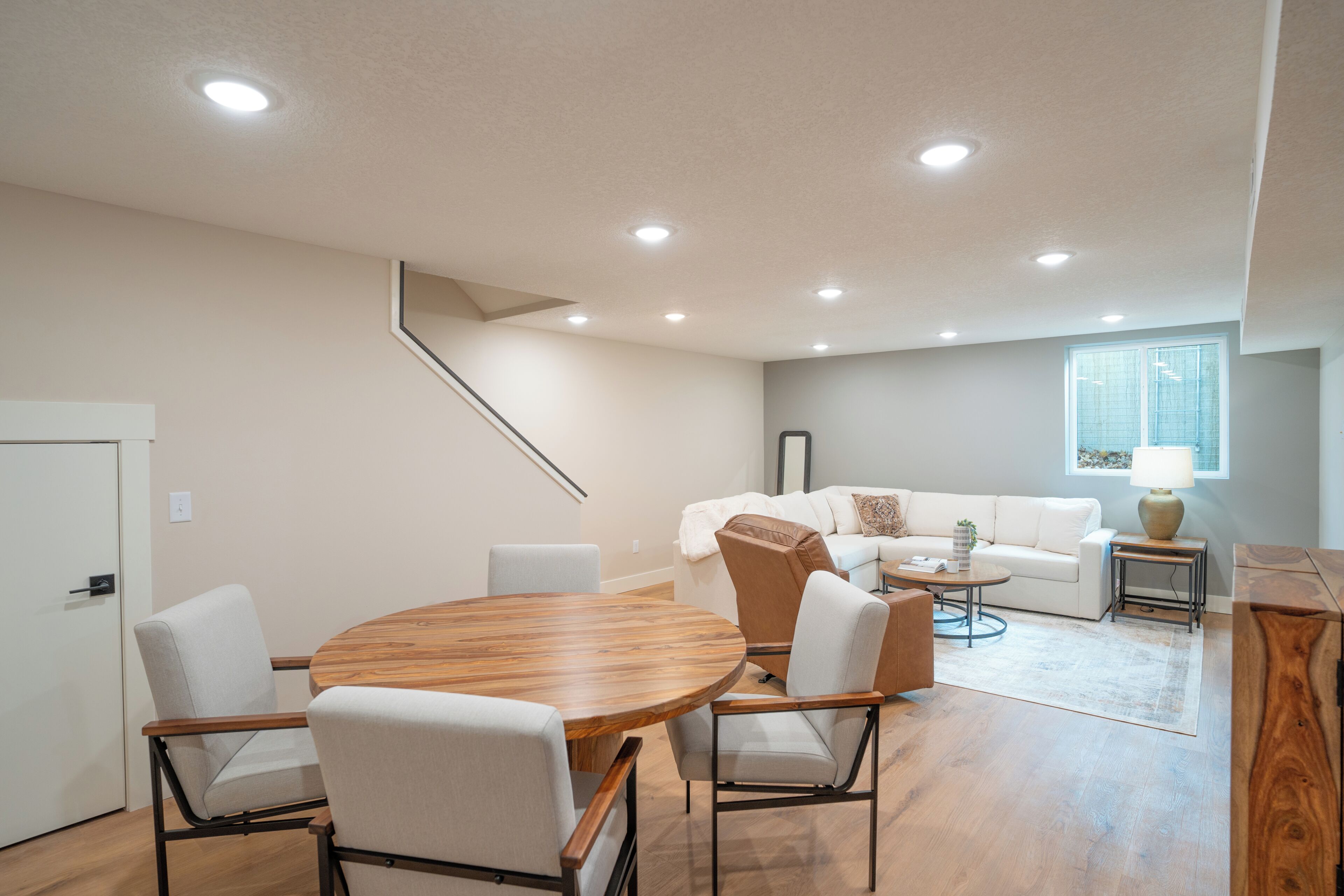 Un salon moderne comprenant un coin repas, un escalier et une fenêtre avec des stores.