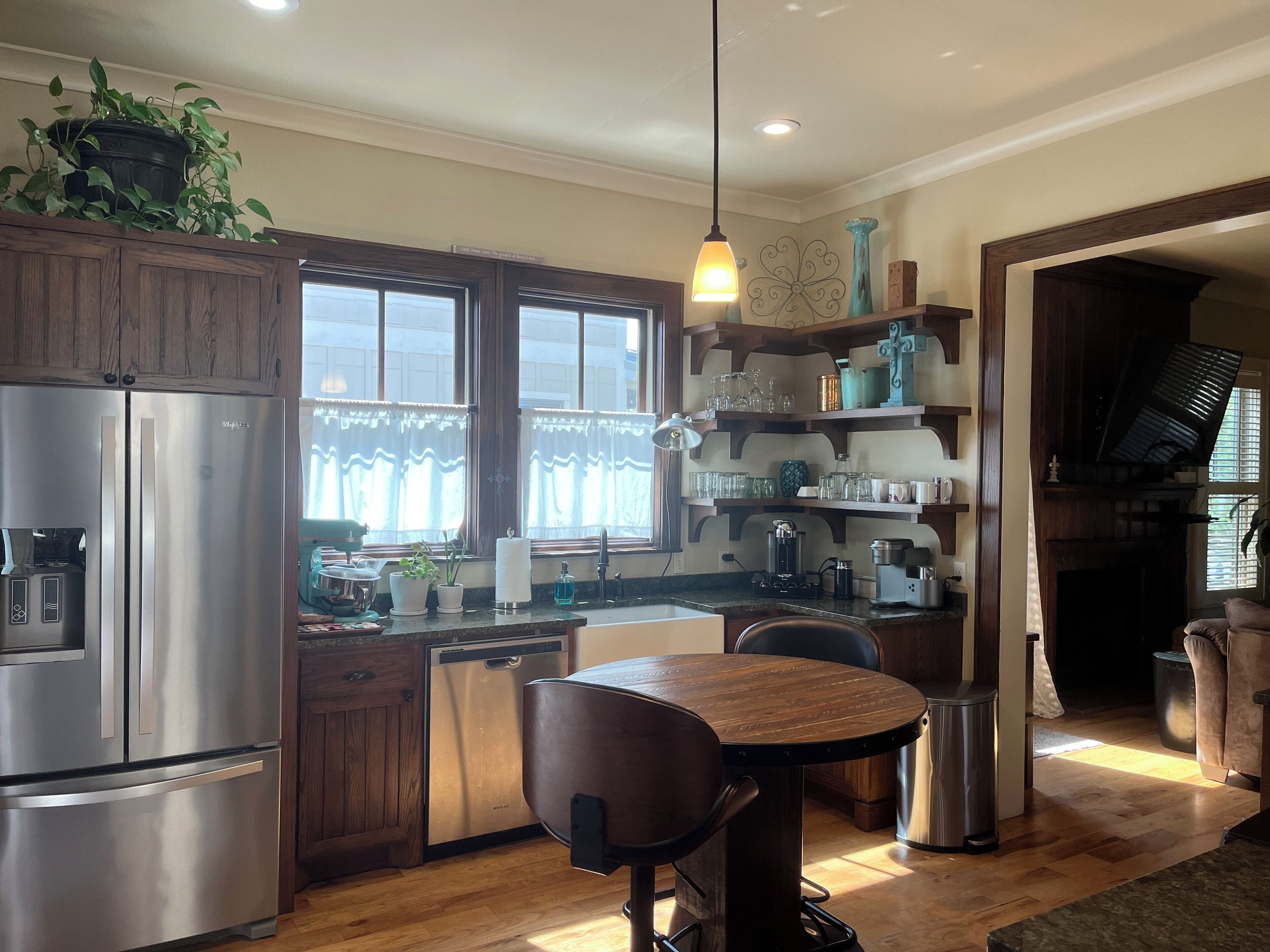 A modern kitchen with stainless steel appliances, wooden cabinets, and a dining area with a round table and bar stools.