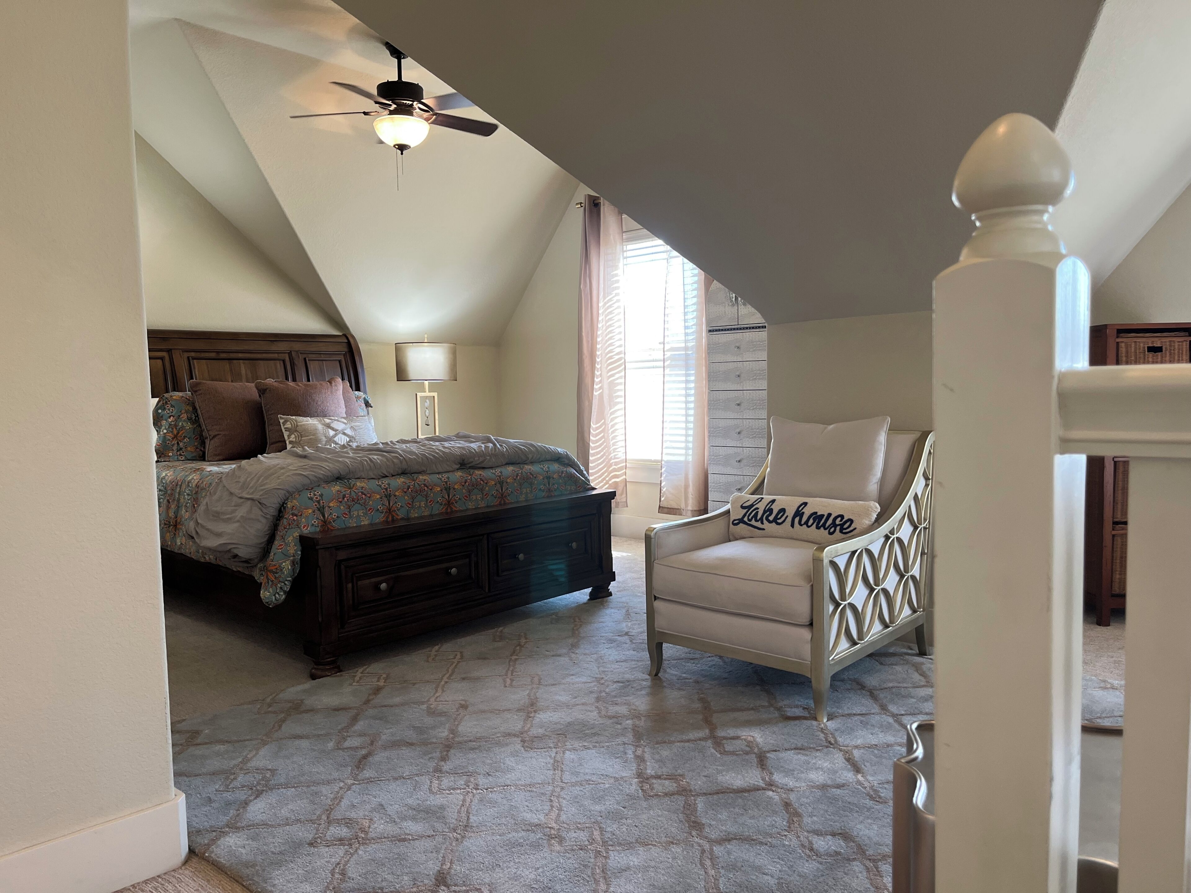 A bedroom with a bed, dresser, chair, and a ceiling fan.