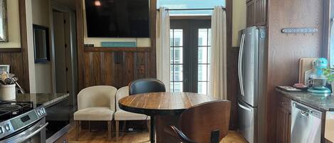 Una cocina moderna con una mesa de comedor de madera, dos sillas, un horno empotrado, un refrigerador y una lámpara colgante.
