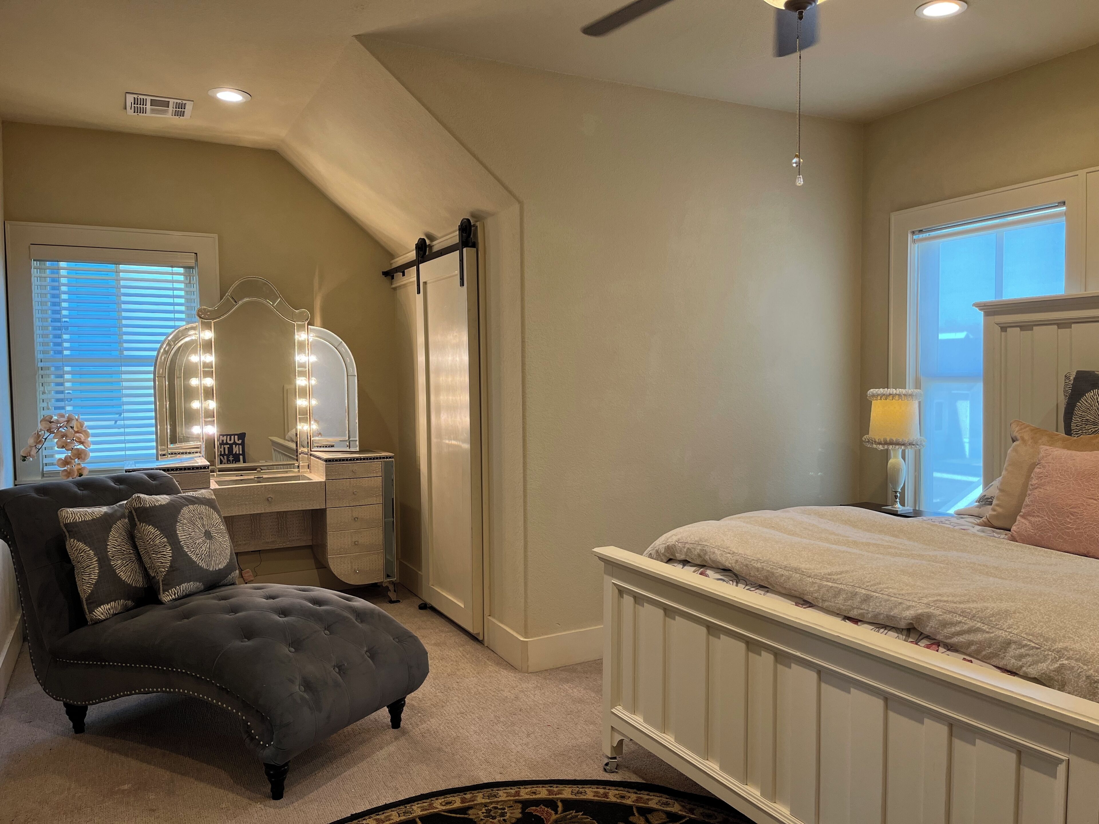 A bedroom with a vanity, a bed, a ceiling fan, and a window with blinds.