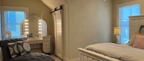 Un dormitorio con tocador, cama, ventilador de techo y ventana con persianas.