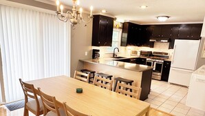 Une cuisine moderne avec des meubles de couleur sombre, un îlot central et un coin repas doté de chaises en bois.