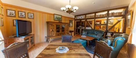 Un salon avec une table à manger en bois, un canapé bleu et un téléviseur posé sur un meuble en bois.