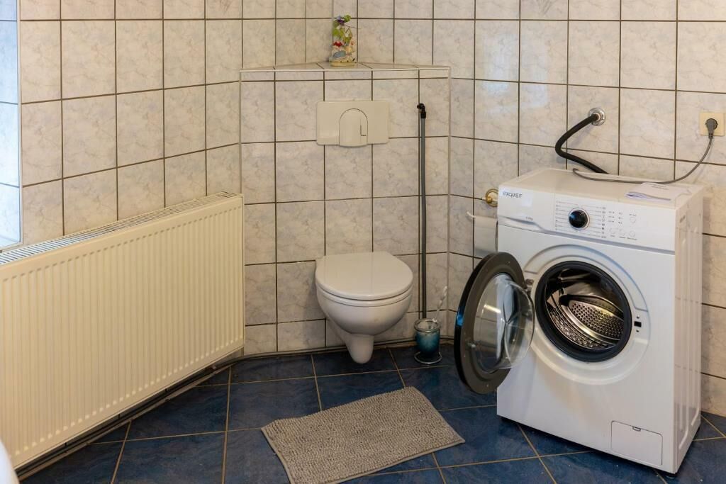 Een kleine badkamer met een toilet, een wasmachine en een radiator.