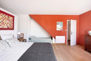A bedroom with a bed, a chair, a desk, a dresser, and a door leading to another room.