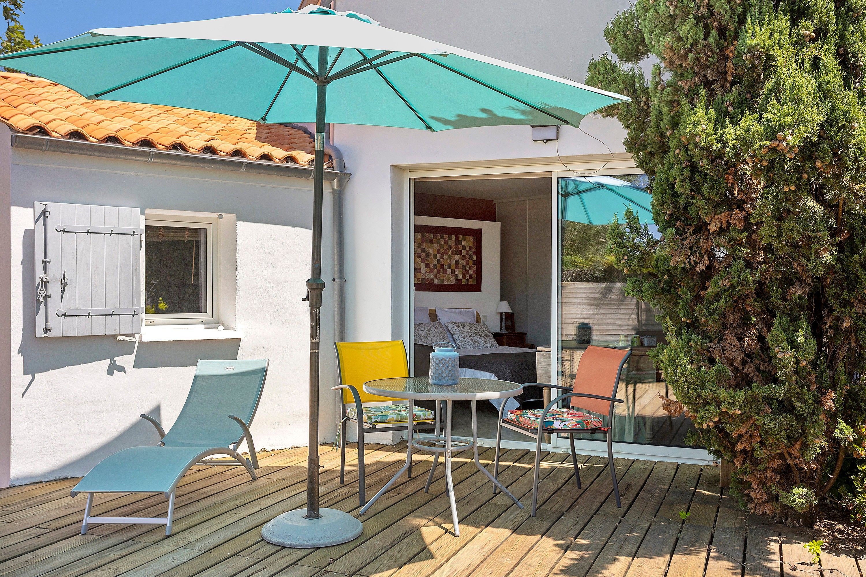 A wooden deck with outdoor furniture, a covered seating area, and a view of a bedroom.