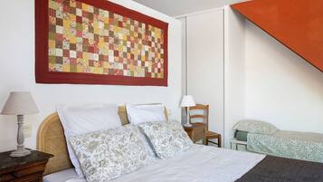 A bedroom with a bed, pillows, a lamp, a chair, and a large quilt hanging on the wall.