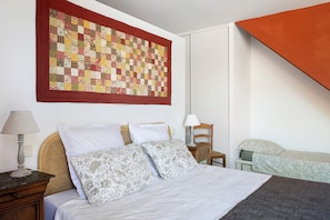 Une chambre à coucher avec un lit, des oreillers, une lampe, une chaise et une grande courtepointe accrochée au mur.