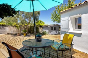 Eine Terrasse mit einem runden Tisch, Stühlen, einem blauen Sonnenschirm und Topfpflanzen.