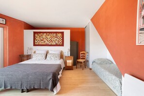 Ein Schlafzimmer mit einem großen Bett, einem kleineren Bett, einem Sessel, einem Nachttisch und einer Wanddekoration.