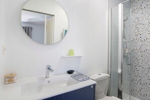Ein Badezimmer mit weißem Waschbecken, einem Spiegel, einer Toilette und einer Duschkabine.