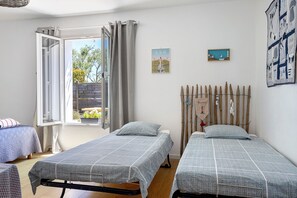 Una habitació amb dos llits individuals, una finestra amb cortines, una tanca de fusta a l'exterior i una paret amb un quadre emmarcat.