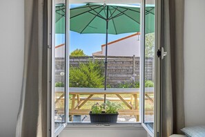 Una porta corredissa de vidre, una paraigua verda, un pont de fusta i plantes en testos.