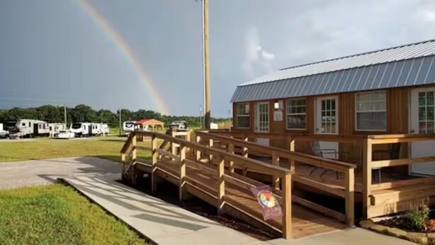 A building with a wooden deck and a sign, surrounded by a grassy area and parked RVs. - Farm Charm Meets Coastal Calm #36 (Elberta)