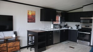 A modern kitchen with dark cabinets, a stainless steel oven, and a flat-screen TV. - Farm Charm Meets Coastal Calm #36 (Elberta)