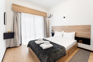 A modern hotel room with a large bed, a bedside table, a wall-mounted air conditioner, and a window with curtains. - GuestReady - Oporto Breiner Terrace (Porto)