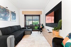 A modern living room with a black sectional sofa, a wooden coffee table, and a large window with a view of the outdoors. - GuestReady - Oporto Breiner Terrace (Porto)