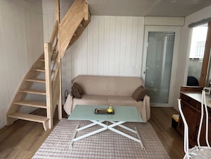 Ein Zimmer mit einer Holztreppe, einem beigen Sofa, einem Glastisch und einem Holzkabinett.