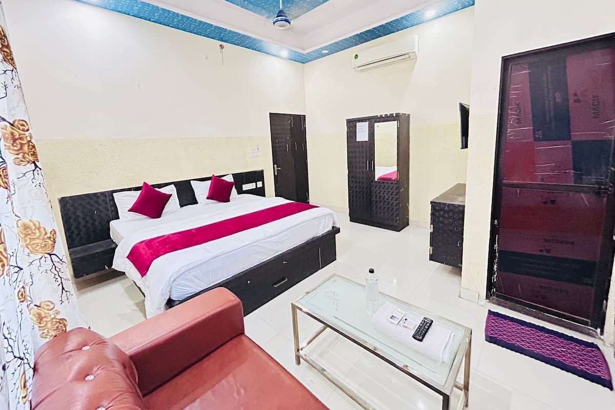 Una habitación de hotel con una cama, una mesa de centro de vidrio, un sofá rojo, un espejo y un equipo de aire acondicionado.