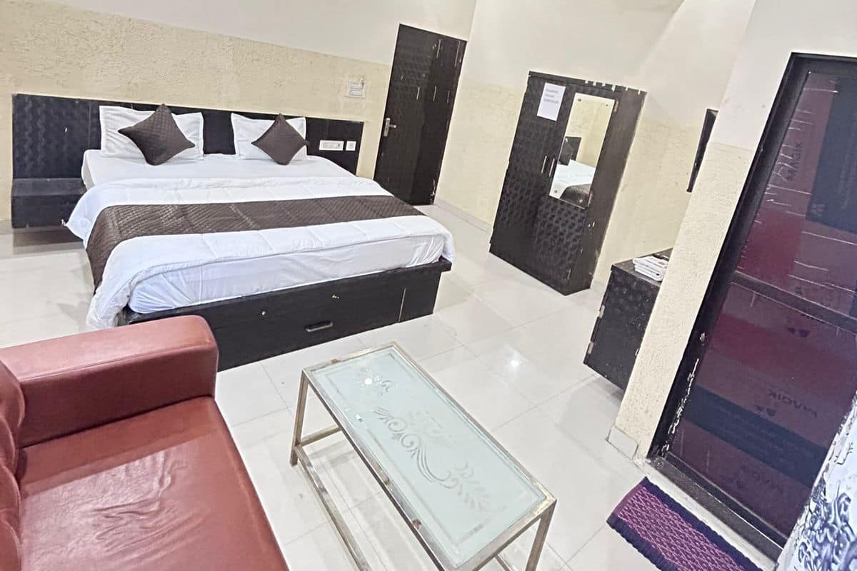 Habitación de hotel con cama, sofá, mesa de vidrio, unidad de aire acondicionado y ventilador de techo.