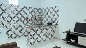 Een kamer met een behang met geometrisch patroon, een flatscreen televisie op een standaard, en een klein plankje met spullen.