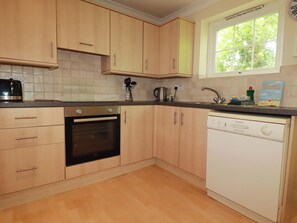 A kitchen with wooden cabinets, a built-in oven, a dishwasher, and a window with a view of greenery. - 20 Atlantic Reach (St. Columb Major)