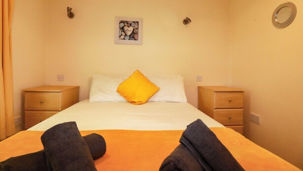 A hotel room with a bed, two nightstands, a wall-mounted picture, and a mirror. - 20 Atlantic Reach (St. Columb Major)