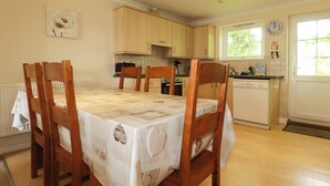 A dining area with a table set for four, wooden chairs, a white tablecloth, and a kitchen in the background. - 20 Atlantic Reach (St. Columb Major)