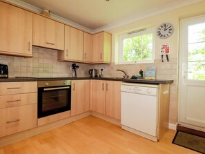 Eine Küche mit Holzausstattung, einem Geschirrspüler, einem Backofen und einem Fenster mit Blick auf Bäume.