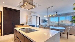 A modern kitchen with a central island, dark wooden cabinets, and a large window overlooking a cityscape. - Luxury Cabo Condo With Multiple Pools, Pickleball, gym & Rooftop (Cabo San Lucas)