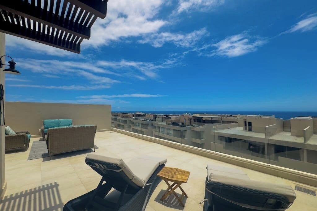 Terraço no telhado com cadeiras de descanso, uma mesa pequena e vista para o mar e edifícios.
