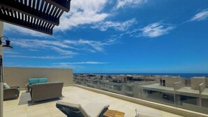 A rooftop terrace with lounge chairs, a small table, and a view of the sea and buildings. - Luxury Cabo Condo With Multiple Pools, Pickleball, gym & Rooftop (Cabo San Lucas)