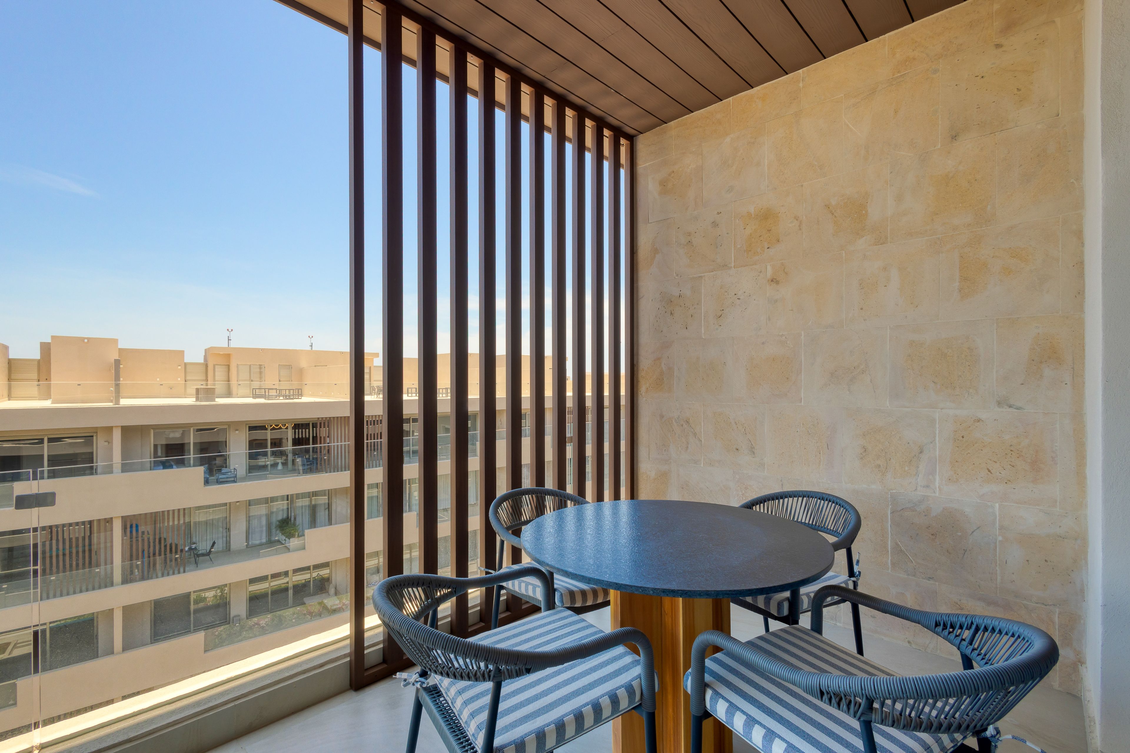 A balcony with a round table and chairs, a stone wall, and a view of other buildings.