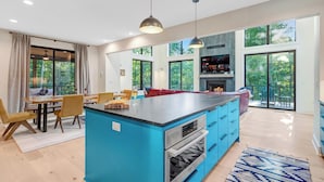 A modern kitchen with a blue island, large windows, and a fireplace.