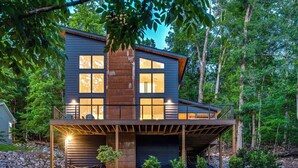 A modern two-story house with a balcony, a stone fireplace, and a stone foundation.