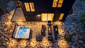 A modern house with a hot tub, outdoor seating, and a stone patio.