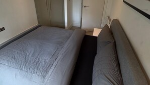 Een slaapkamer met een bed, een kledingkast, een deur en een lijst met een afbeelding aan de muur.